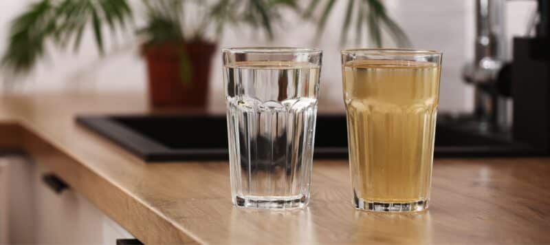 two glasses of water sitting on a wooden table, one of them clean and clear and the other one filled with murky dirty water