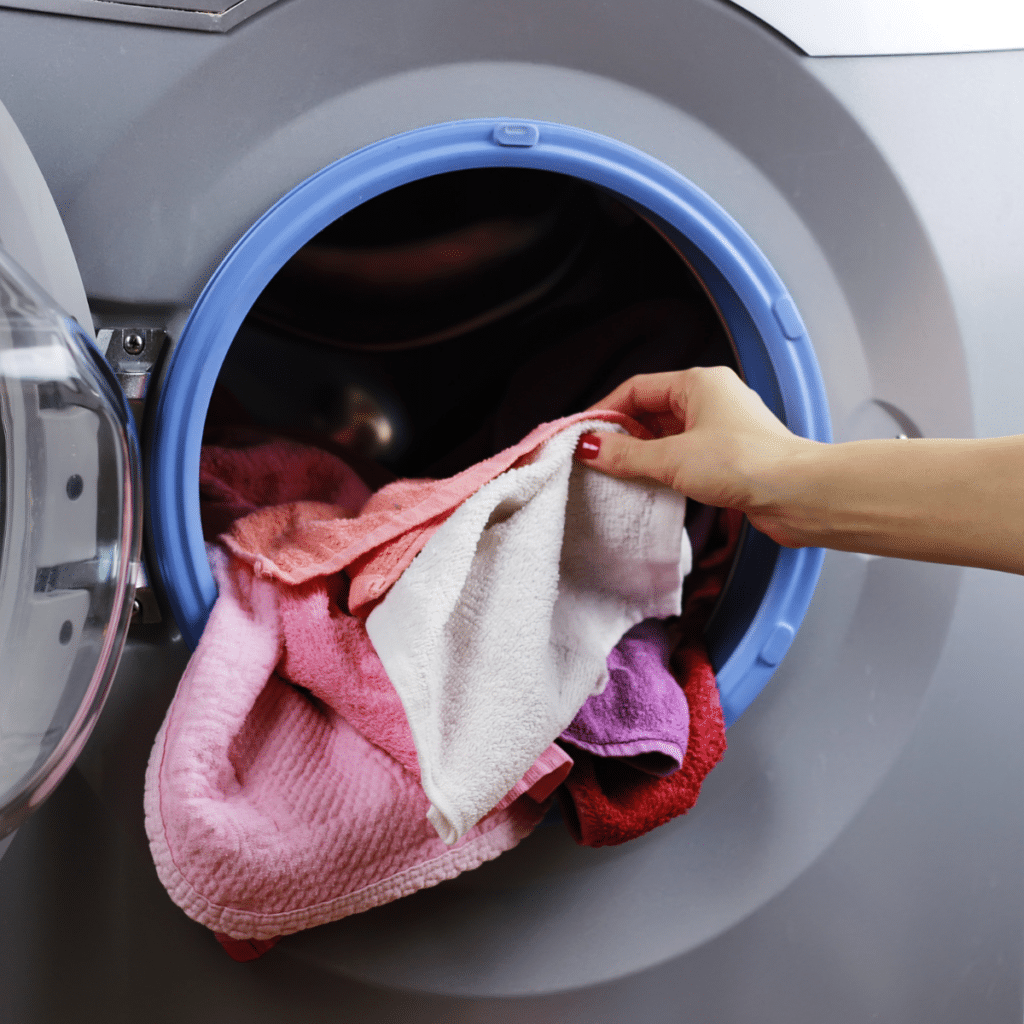 A hand reaching into a washing machine to retrieve pink towels